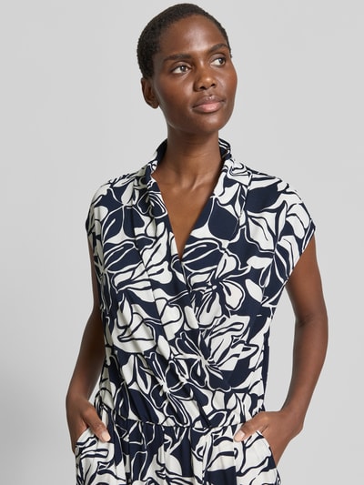 Frauenmodel trägt Jumpsuit mit Schalkragen und Kappärmeln von Betty Barclay, Material-Mix mit Stretch-Anteil, abstraktes Blumenmuster, Taillierter Schnitt, Nahaufnahme Oberkörper.
