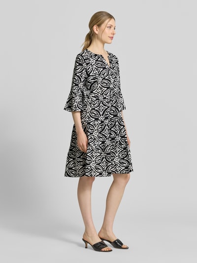 Frauenmodel trägt Minikleid mit Tunika-Ausschnitt von Christian Berg Woman Selection, Schwarz-Weiß-Muster, reine Baumwolle, taillierte Passform, Halbarm, Ganzkörperansicht von vorne.