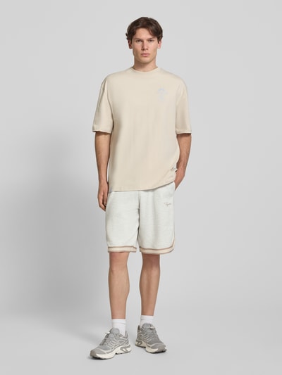 Männermodel trägt Shorts mit Strukturmuster und Label-Stitching von PEGADOR aus reiner Baumwolle im Regular-Fit, Eingrifftaschen, elastischer Bund, helles Beige, Textur sichtbar, Ganzkörperansicht von vorne.