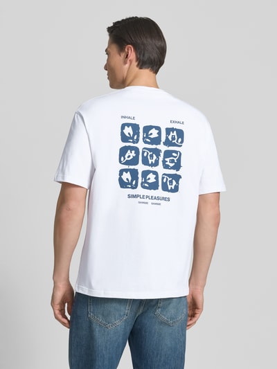 Męski model nosi T-Shirt mit Label-Print Modell 'COHEN' od Samsøe Samsøe z czystej bawełny organicznej, krój relaxed fit, biały z niebieskim nadrukiem, okrągły dekolt, długość tyłu w rozmiarze M: 71 cm, widok całej sylwetki z tyłu.