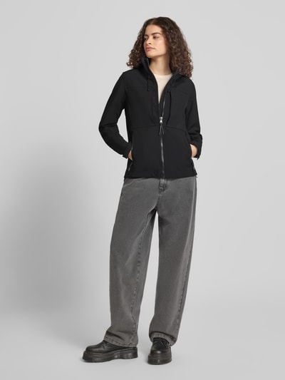 Frauenmodel trägt Trekker Jacke mit Kapuze und Label-Patch von Superdry aus schwarzem Material-Mix mit Stretch-Anteil, Gerader-Schnitt, Kapuze mit Kordelzug, Stehkragen, Reißverschluss, Logo-Stitchings, Label-Patch, seitliche Reißverschlusstaschen, verstellbare Ärmelriegel mit Klettverschluss, Ganzkörperansicht von vorne.