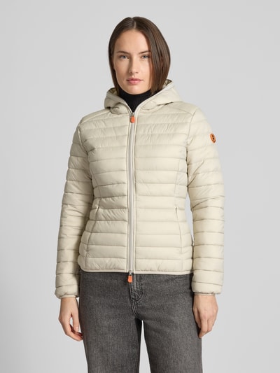 Frauenmodel trägt Steppjacke mit Kapuze Modell 'DAISY' von SAVE THE DUCK, cremefarben, körpernahe Passform, Ganzkörperansicht von vorne.