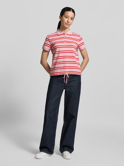 Frauenmodel trägt Regular Fit Poloshirt aus Baumwoll-Mix von Tommy Hilfiger, Optik: Unifarben, Muster: Gestreift, Logo-Detail, Polokragen, kurze Knopfleiste, Kurzarm, Ärmelabschluss: Gerippt, Rumpfabschluss: Tunnelzug, Materialverarbeitung: Piqué, Material: Baumwoll-Mix, sanfte Farben, glatte Textur, Ganzkörperansicht von vorne.