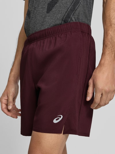 Männermodel trägt Shorts mit elastischem Bund und Logo von ASICS in Dunkelrot, glatte Textur, seitlicher Logo-Print, Nahaufnahme Oberschenkel, Regular Fit, Innenhose, Bundweite 37 cm, Innenbeinlänge 45 cm.