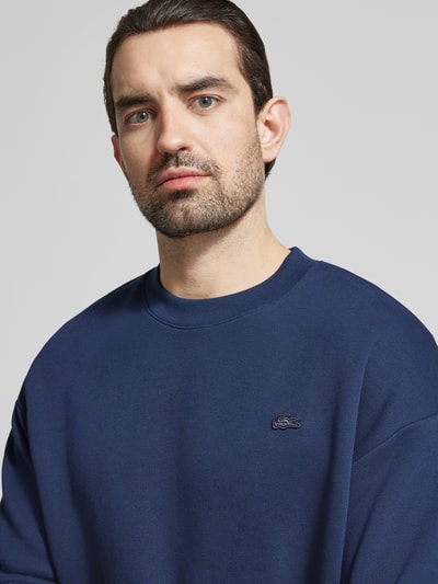 Männermodel trägt Relaxed Fit Sweatshirt aus reiner Baumwolle von Lacoste, Optik: Unifarben, Logo-Stitching, Nahaufnahme Oberkörper.