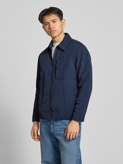 Männermodel trägt Regular Fit blouson met platte kraag van Marc O'Polo Denim, look: effen, waterafstotend, borstzak met drukknoop, steekzakken, lange mouw, ritssluiting, labelapplicatie, kleur donkerblauw, textuur glad, materiaal glanzend, pasvorm regular fit, sluiting ritssluiting, zijaanzicht, Ganzkörperansicht von vorne.