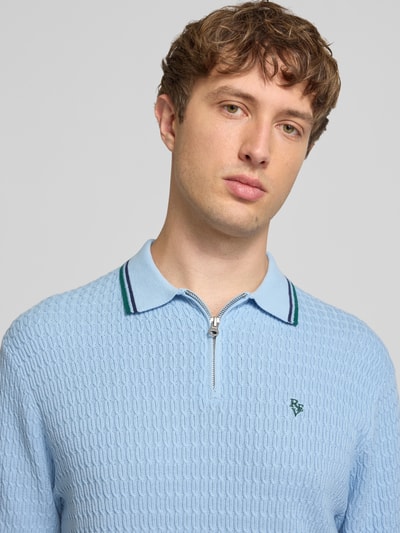 Männermodel trägt Slim Fit Poloshirt in Strick-Optik von REVIEW in Hellblau mit Polokragen, Reißverschluss, Logo-Stitching, Nahaufnahme Oberkörper.