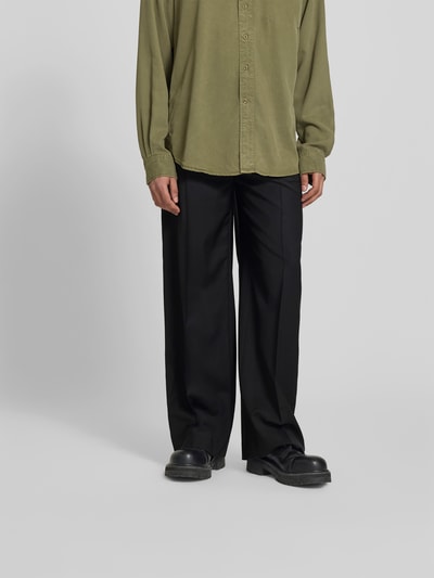 Männermodel trägt Wide Fit Stoffhose aus Woll-Mix von Filippa K, schwarz, Bügelfalten, Gesäßtaschen, Knopf-Reißverschluss, Nahaufnahme Unterkörper, ganz leicht von vorne.