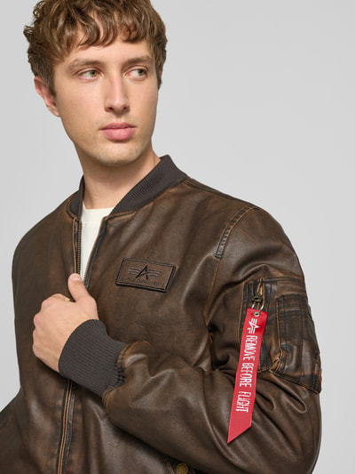 Männermodel trägt Bomberjacke in Leder-Optik mit Label-Details von Alpha Industries, braun, Reißverschluss, Nahaufnahme Oberkörper. Herren Bomberjacke von Alpha Industries, Regular Fit, Kapuze, Stehkragen, Rückenlänge M 63 cm, Schulterbreite M 44 cm, Brustweite M 52 cm, Ärmellänge M 60 cm.