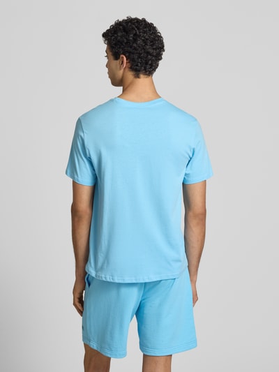 Männermodel trägt T-Shirt mit Logo und Rundhalsausschnitt von CHAMPION in Hellblau, reine Baumwolle, Regular Fit, Rückansicht Ganzkörperansicht.