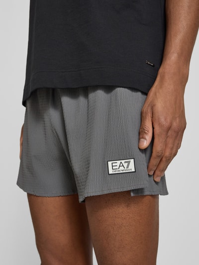 Männermodel trägt Relaxed Fit Shorts mit integriertem Slip von EA7 Emporio Armani, Strukturmuster, Logo-Patch, Elastischer-Material-Mix, Nahaufnahme Oberschenkel.