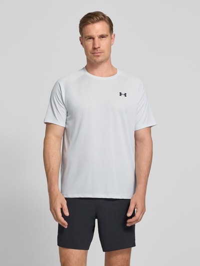 Männermodel trägt Under Armour Herren T-Shirt mit Label-Print Modell 'Tech' in Hellgrau, Gerader-Schnitt, Rundhalsausschnitt, Ganzkörperansicht von vorne. Rückenlänge bei Größe M: 75 cm.