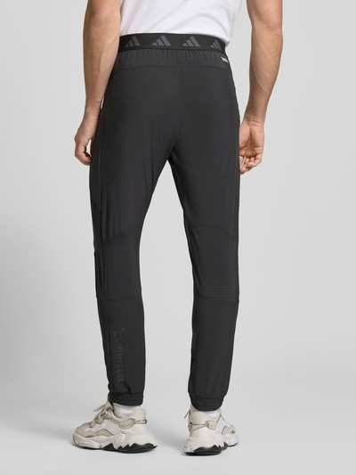 Männermodel trägt schwarze Regular Fit Trackpants mit elastischem Logo-Bund von adidas Training, Ganzkörperansicht Rückansicht.