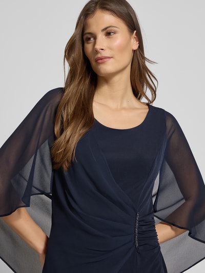 Frauenmodel trägt knielanges Cocktailkleid mit Rundhalsausschnitt von Vera Mont in Dunkelblau, Wickel-Optik, Strasssteinbesatz, Chiffonfledermausärmel, Nahaufnahme Oberkörper.