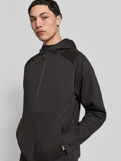 Männermodel trägt Regular Fit Sweatjacke mit Kapuze Modell 'Base' von Jack & Jones in Schwarz, elastischer Material-Mix, Reißverschlusstaschen, Nahaufnahme Oberkörper.