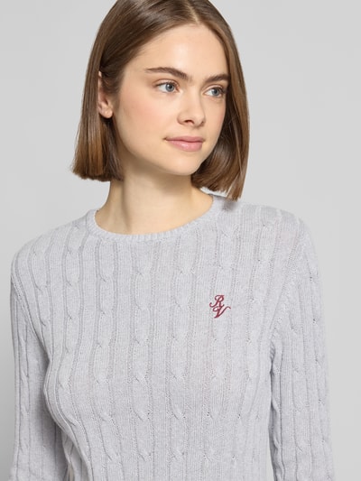 Frauenmodel trägt Strickpullover mit Zopfmuster und Label-Stitching von REVIEW aus Baumwoll-Mix, Regular-Fit, Rundhalsausschnitt, Nahaufnahme Oberkörper.