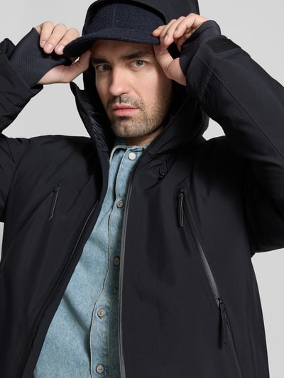 Männermodel trägt Daunenjacke mit Daunen-Feder-Füllung von MM6 Maison Margiela in Schwarz, Label-Print, Zweiwege-Reißverschluss, Reißverschlusstaschen, Kapuze mit Kinnschutz, lockere Passform, Nahaufnahme Oberkörper.