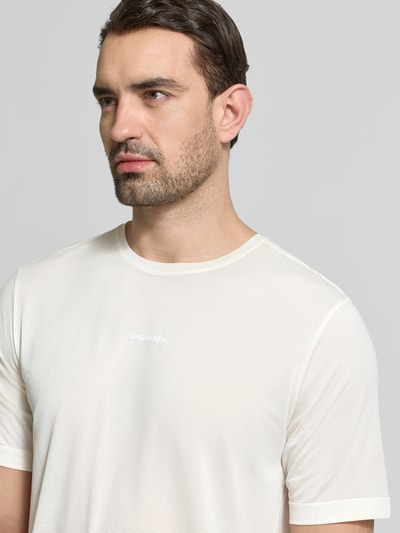 Männermodel trägt Funktionsshirt mit Rundhalsausschnitt und Logo von Salomon, Regular Fit, hell, glatte Textur, Nahaufnahme Oberkörper.
