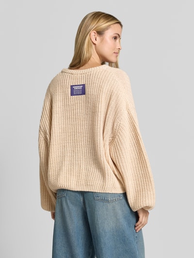 Vrouwenmodel draagt oversized gebreide pullover uit linnenmix van American Vintage, beige tint, met lange mouwen, geribde zoom, ruglengte maat XS/S 56 cm, mouwlengte 54 cm, detailopname van achteraan.