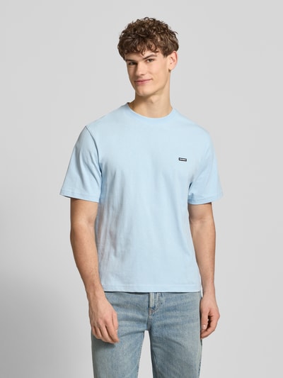 Männermodel trägt Basic T-Shirt mit kleinem Logo-Patch auf der Brust von REVIEW in Hellblau, Baumwolle, gerader Schnitt, Ganzkörperansicht von vorne.