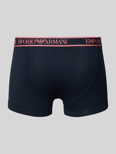 Männermodel trägt Slim Fit Trunks mit Logo-Stitching im 3er-Pack von Emporio Armani in Dunkelblau und Pink, Ganzkörperansicht Rückansicht.