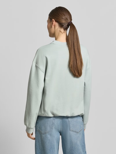 Frauenmodel trägt Sweatshirt mit Knopfleiste Modell 'Tessina' von JOOP! in hellem Blau, lockere Passform, Ganzkörperansicht Rückansicht.