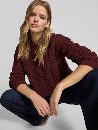 Frauenmodel trägt Regular Fit Strickpullover mit Zopfmuster Modell 'ELLY' von Only in Dunkelrot, unifarben, Cropped, Nahaufnahme Oberkörper.