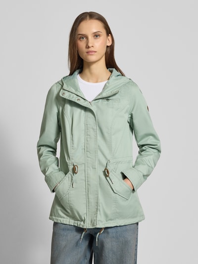 Kobiece model prezentuje Regular Fit Parka mit Baumwoll-Anteil Modell 'LORCA' od Only, gładki canvas w miętowym kolorze, długo rękaw, kaptur, patki na kieszeniach, detal label patch, przód z krytym zamkiem i guzikami, krój regular fit, widok całej sylwetki z przodu.