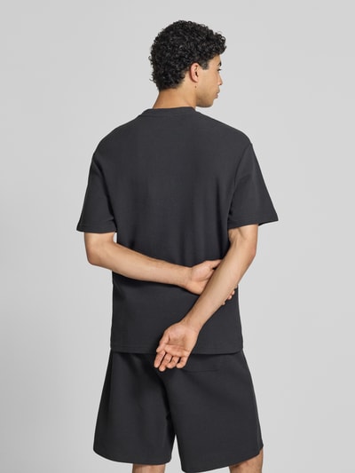 Männermodel trägt Oversized T-Shirt mit Strukturmuster und Logo-Stitching von KARL KANI aus Baumwoll-Mix, Oversized-Fit, Rückenlänge 75 cm, Ganzkörperansicht Rückansicht.