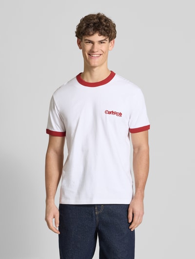 Männermodel trägt weißes T-Shirt im Retro-Look mit rotem Label-Print von Carhartt Work In Progress, Baumwolle, Regular Fit, Ganzkörperansicht von vorne.