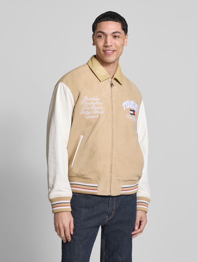 Männermodel trägt Relaxed Fit College-Jacke aus echtem Leder von Tommy Jeans in Lederoptik mit Label-Schriftzug, Glattleder und Veloursleder, Kontrastfarben, Umlegekragen, Reißverschluss und seitlichen Paspeltaschen, Ganzkörperansicht von vorne.