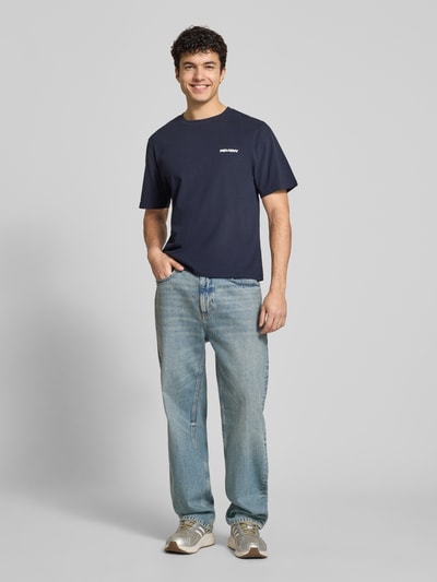Männermodel trägt T-Shirt mit Logo und Rundhalsausschnitt von REVIEW aus Baumwoll-Viskose-Mix, Regular-Fit, dunkelblau, Ganzkörperansicht von vorne. Rückenlänge bei Größe M: 64 cm.