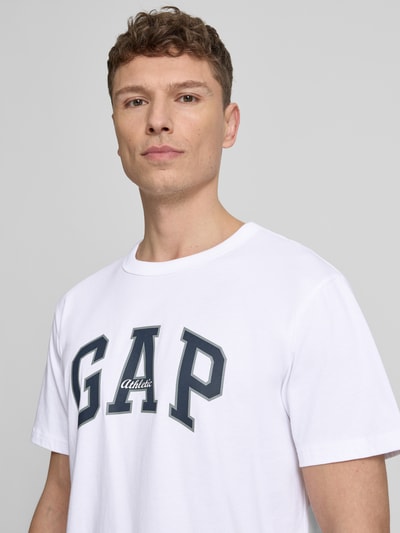 Männermodel trägt T-Shirt mit Logo und Rundhalsausschnitt von GAP in Weiß, Regular-Fit aus reiner Baumwolle, Nahaufnahme Oberkörper.