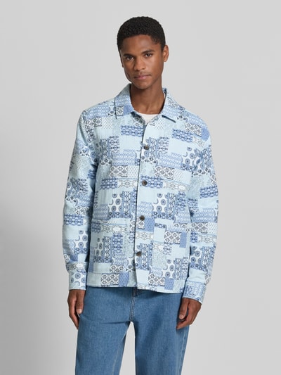 Męski model nosi Regular Fit Overshirt im Allover-Look od Les Deux, bawełniany miks, niebieskie wzory patchwork, kołnierzyk kent, zapięcie na guziki, długość pleców w rozmiarze M: 69 cm, krój regular fit, widok całej sylwetki z przodu.