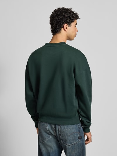Männermodel trägt Oversized Sweatshirt mit Label-Detail von PROHIBITED in Dunkelgrün aus Baumwoll-Mix, Gerippte-Abschlüsse, Rückenlänge 68 cm, Ärmellänge 70 cm, Ganzkörperansicht Rückansicht.