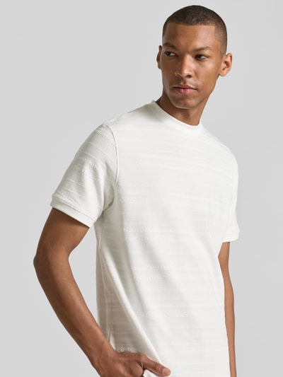 Mannenmodel draagt T-shirt met structuurpatroon en ronde hals van guess in katoenmix, regular fit, ruglengte maat M 74 cm, detailopname bovenlichaam.