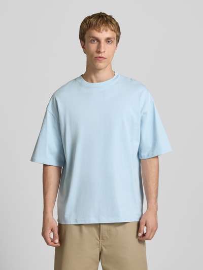 Męski model nosi Oversized T-Shirt mit Logo od REVIEW, jasnoniebieska bawełna, krój oversize, logo, okrągły dekolt, widok z przodu całej sylwetki.