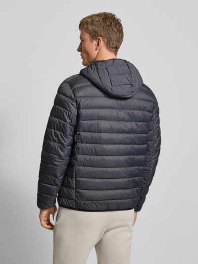 Männermodel draagt gewatteerd jack met capuchon en logoprint, regular fit, steekzakken, ritssluiting, CHAMPION, ruglengte 71 cm, schouderbreedte 51 cm, borstwijdte 61 cm, mouwlengte 69 cm. Ganzkörperaanzicht rugzijde.