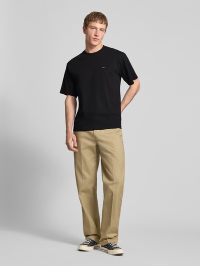 Männermodel trägt T-Shirt mit Label-Detail und Rundhalsausschnitt von Dickies, Schwarz, Reine Baumwolle, Relaxed-Fit, Rückenlänge 70 cm, Ganzkörperansicht von vorne.