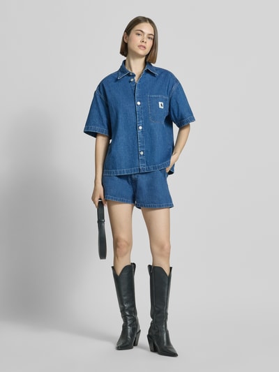 Frauenmodel trägt Shorts in Denim-Optik Modell 'Lova' von Carhartt Work In Progress aus Reine Baumwolle, ausgestellte Passform, Eingriffstaschen, Gesäßtaschen, Knopf- und Reißverschluss, Bundweite 38 cm, Innenbeinlänge 6 cm, Ganzkörperansicht von vorne.