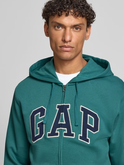 Männermodel trägt Sweatjacke mit Logo und Känguru-Tasche von GAP in Grün; Baumwoll-Mix, Regular Fit, Nahaufnahme Oberkörper.