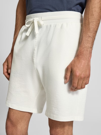 Männermodel trägt Loose Fit Sweatshorts aus Bio-Baumwoll-Mix Modell 'KIAN' von Only & Sons in weißer Piqué-Struktur, Nahaufnahme Oberschenkel.