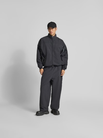 Männermodel trägt dunkelgraue Sweatpants mit elastischem Bund von VETEMENTS, Relaxed-Fit, Eingrifftaschen, Beinabschlüsse mit Tunnelzug, Wide Leg, Innenbeinlänge 70 cm, Bundweite 44 cm, Ganzkörperansicht von vorne.