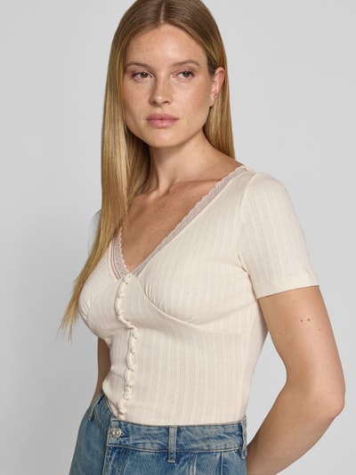 Frauenmodel trägt T-Shirt mit Spitzenbesatz und Knopfleiste von Jake*s Casual, Material-Mix mit Stretch-Anteil, Slim Fit, V-Ausschnitt, Rückenlänge bei Größe S 33 cm, cremefarben mit Rippstruktur und kurzen Ärmeln, Nahaufnahme Oberkörper.