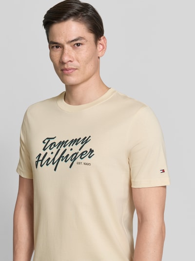 Männermodel trägt Regular Fit T-Shirt aus reiner Baumwolle von Tommy Hilfiger in Beige, unifarben, Label Print, Nahaufnahme Oberkörper.