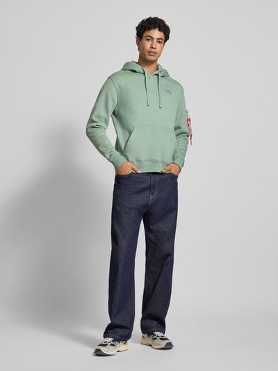 Männermodel trägt Hoodie mit Känguru-Tasche von Alpha Industries, mintgrün, Baumwoll-Mix, Regular-Fit, Label-Patch, Ganzkörperansicht von vorne.