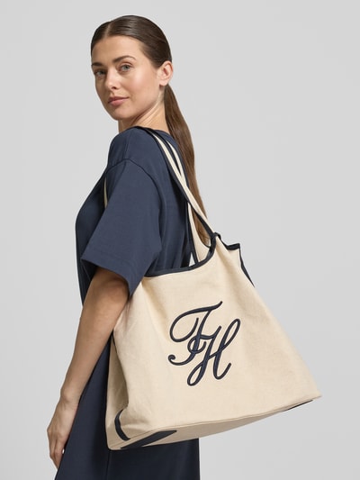 Vrouwenmodel draagt strandtas uit mix van katoen en linnen van Tommy Hilfiger, effen kleuren, magneetsluiting, gestikt logo, contrasterende details, draagband, hoofdvak met afneembaar etui, materiaalverwerking canvas, zijaanzicht bovenlichaam.
