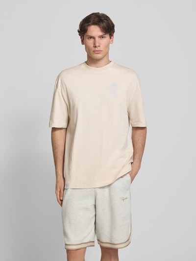 Mężczyznę model prezentuje męski t-shirt z bawełny Pegador Oversized T-Shirt mit rückseitigem Print Modell 'Pedroche', okrągły dekolt, krój oversized fit, nadruk z logo i motywem na plecach, beżowe odcienie, gładka tekstura, długość tyłu w rozmiarze M: 71 cm; całkowity widok z przodu