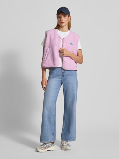 Frauenmodel trägt Weste mit Rundhalsausschnitt Modell 'HOKTOWN' von American Vintage in Rosa mit Druckknopfleiste und Teddyfell, ganzkörperansicht von vorne.