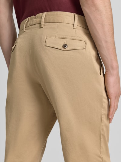 Mężczyzna nosi chinosy Chino mit Eingrifftaschen von Christian Berg Men z mieszanki bawełny i elastanu, krój regular fit, beżowe, widok z tyłu, detal z wpuszczanymi kieszeniami i kieszenią z tyłu, szerokość w rozmiarze 50: 43 cm, długość wewnętrzna nogawki w rozmiarze 50: 82 cm, tekstura gładka. Zbliżenie tylnej części.